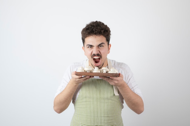 Portrait of hungry male cook holding raw mushrooms on white 