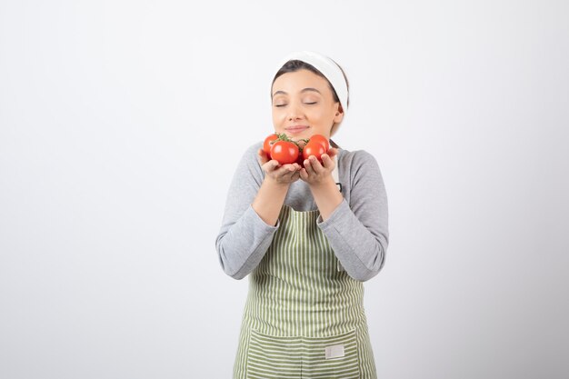 Portrait of hungry woman smells red tomatoes over white wall