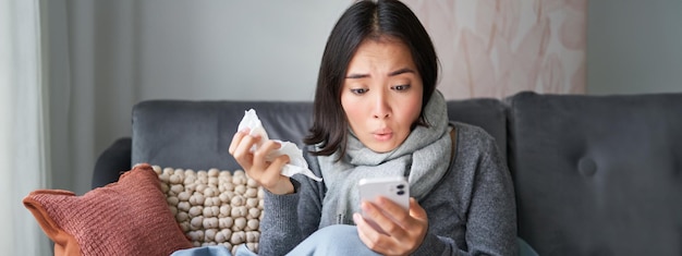 Free photo portrait of ill woman looking at smartphone looking concerned and shocked at mobile phone reading