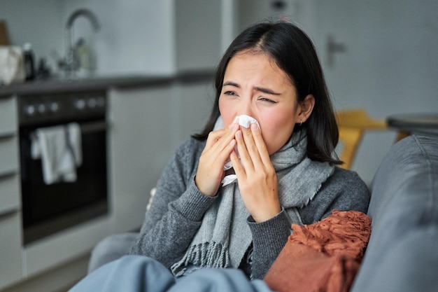 Free photo portrait of ill young korean woman feeling sick sneezing and holding napkin staying at home ill caug