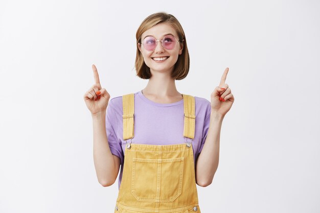 Portrait of impressed and intrigued attractive blonde stylish sunglasses pointing up