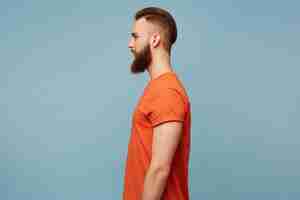 無料写真 ファッショナブルな髪型と剃った頭と青で隔離された横に立っている赤いtシャツの長く厚いひげを持つ男のプロフィールの肖像画