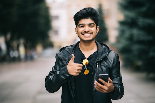 Portrait of indian man in coat typing message on the phone on the city street