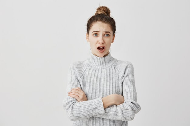 Portrait of indignant adult girl standing in closed posture with mouth opened. Female hipster resenting her friend have done standing with hands crossed. Expressions concept