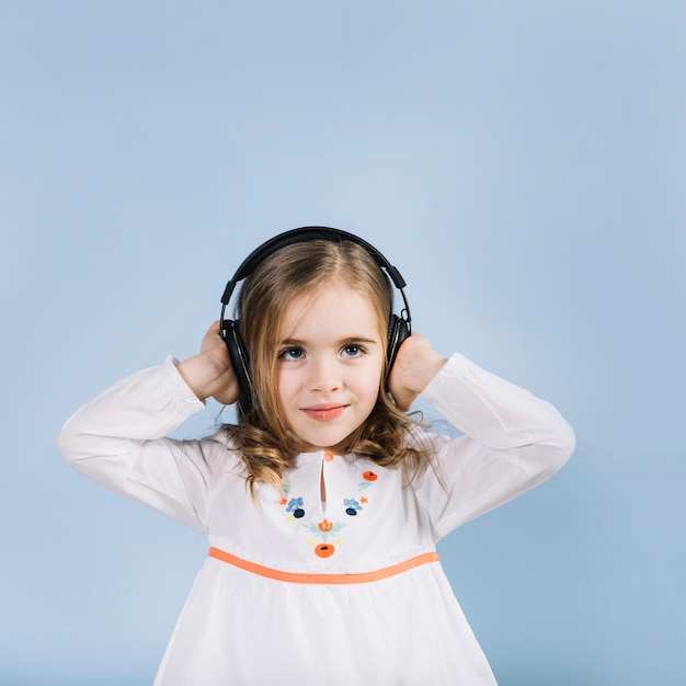 Portrait of a innocence girl listening music on headphone standing against blue background