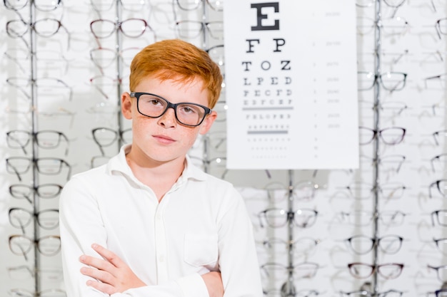 Foto gratuita il ritratto del ragazzo innocente con il braccio ha attraversato la posa al deposito di ottica