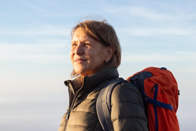 Free photo portrait of inspired elderly woman with orange backpack. sporty woman in casual clothes looking forward with smile. sport, adventure, hobby concept