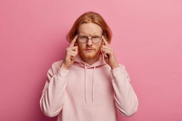 Portrait of intense redhead man presses index fingers on temples