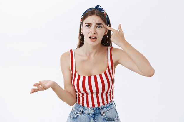 Portrait of irritated and annoyed fed up woman in stylish striped top and headband arguing holding finger on temple looking at crazy guy making stupid mistake