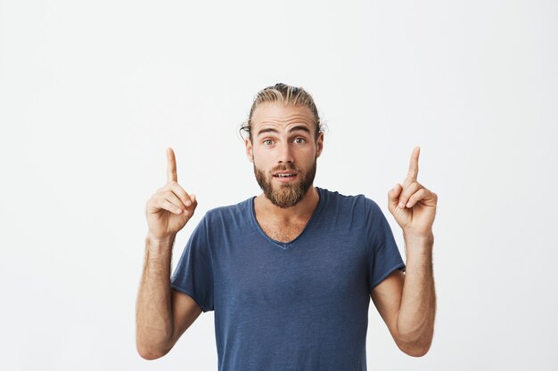 Portrait of joyful beautiful men with fashionable hairstyle and beard, pointing up