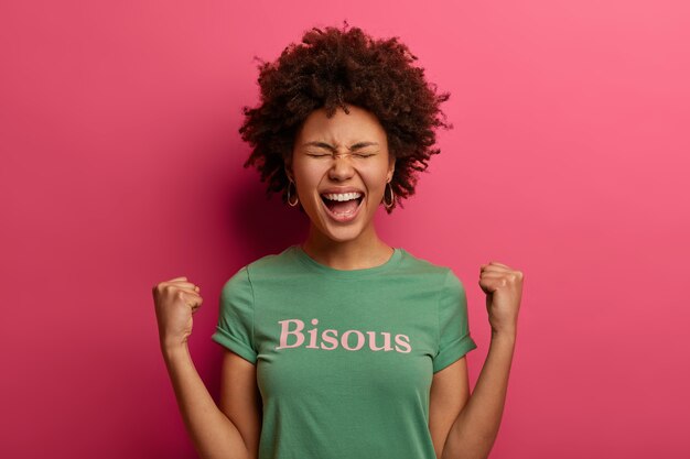 Portrait of joyful curly haired young woman exclaims with joy