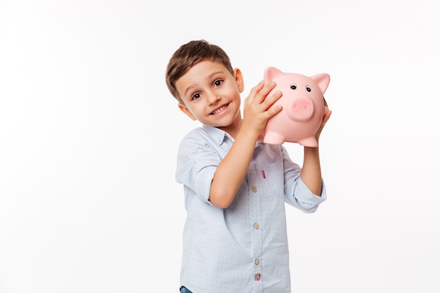 Portrait of a joyful cute little kid holding piggy bank