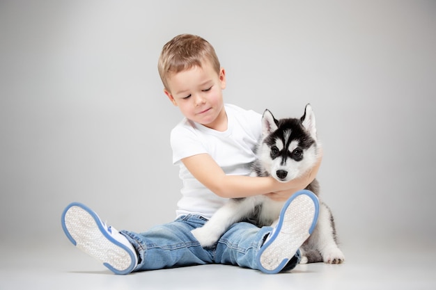 Portrait of a joyful little boy having fun with siberian husky puppy on the floor at studio. The animal, friendship, love, pet, childhood, happiness, dog, lifestyle concept