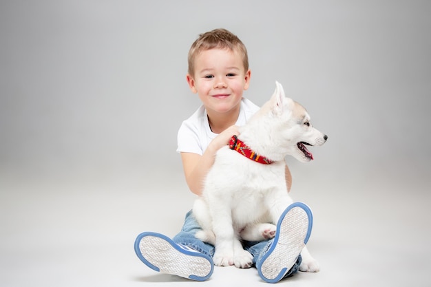 스튜디오 바닥에서 시베리안 허스키 강아지와 즐거운 시간을 보내는 어린 소년의 초상화. 동물, 우정, 사랑, 애완 동물, 어린 시절, 행복, 개, 라이프 스타일 개념