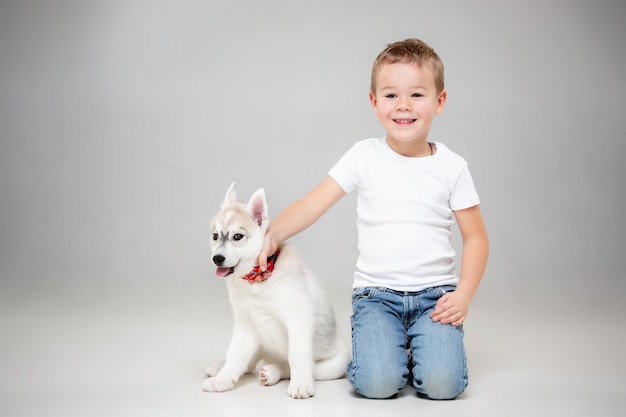 Portrait of a joyful little boy having fun with siberian husky puppy on the floor at studio.