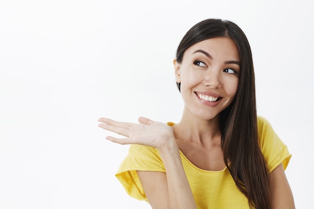 Portrait of joyful pleased cute european female with dark hair in trendy yellow t-shirt stooping pointing left