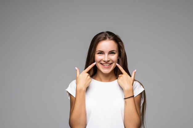 Portrait of joyful satisfied woman gesturing her beaming white healthy teeth on grey