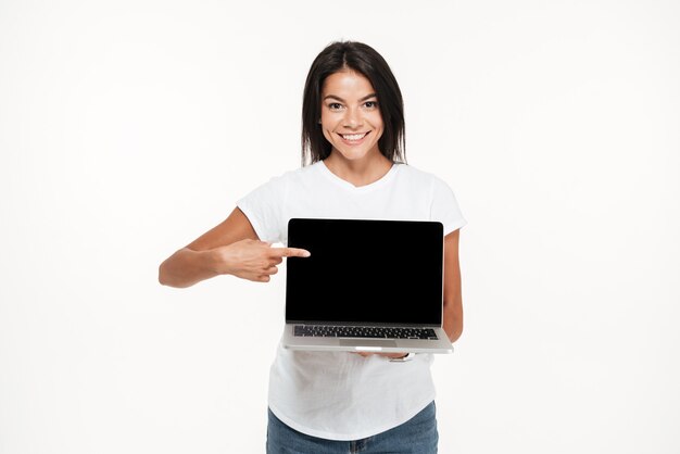Portrait of a joyful young woman holding blank screen laptop