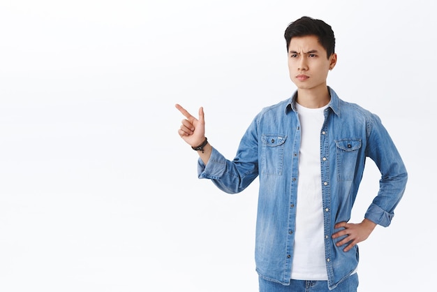 Portrait of judgemental seriouslooking angry young man dont approve bad thing seeing something disappointing pointing and looking left with aversion disapprove white background