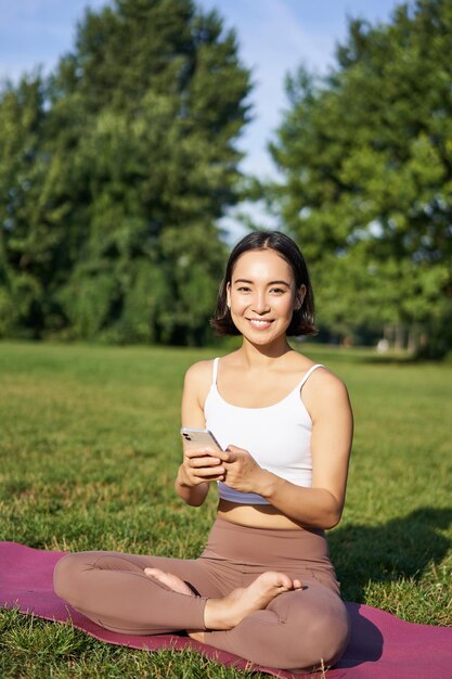 Portrait of korean girl meditating in park follow yoga video lesson on smartphone app sitting on fre