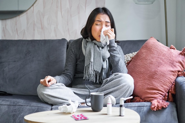 Free photo portrait of korean woman sneezing feeling sick staying at home with flu or cold neck wrapped with sc