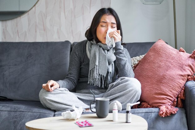 Portrait of korean woman sneezing feeling sick staying at home with flu or cold neck wrapped with sc