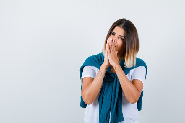 Portrait of lady with tied sweater with hands in praying gesture in white t-shirt and looking hopeful front view