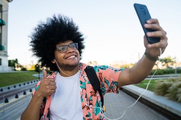 Portrait of latin man taking a selfie with his mobile phone while standing outdoors on the street.