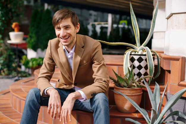 Portrait laughing young relaxed man sitting outdoors on vintage circular stairs