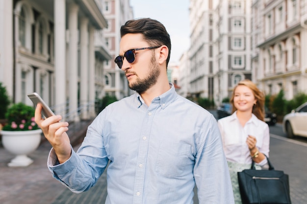 Portrait of a little bit sad gut in sunglasses looking on phone on street. Pretty blonde girl catching him