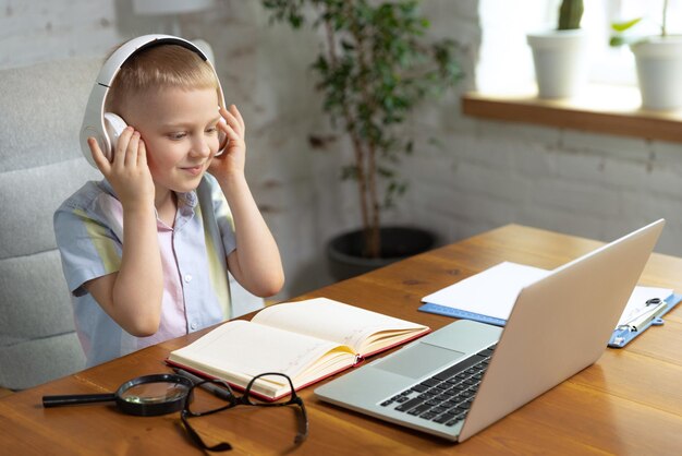 Portrait of little boy child in headphones studying at home looking on laptop working with teacher Online education