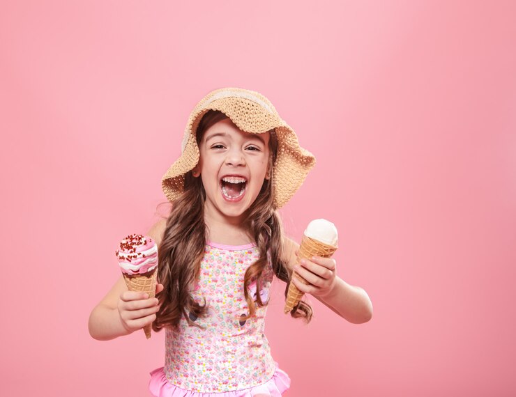 A young girl in a swimsuit happily holds two ice cream cones from a soft serve ice cream machines.