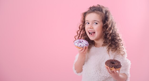 Portrait of a little curly girl eating donuts