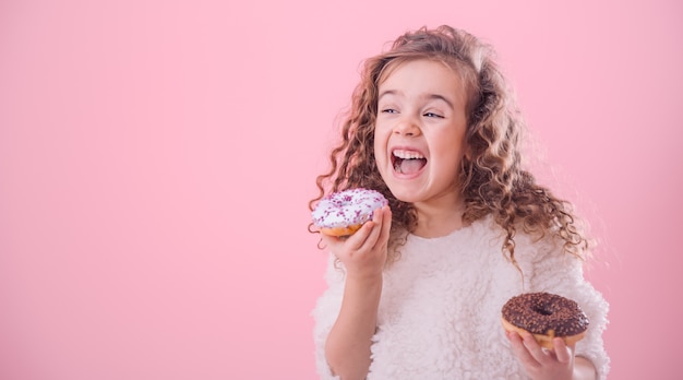 Portrait of a little curly girl eating donuts