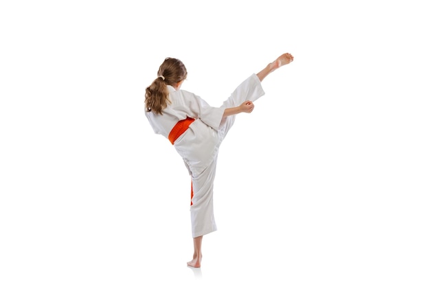 Portrait of little girl, child in kimono training karate isolated on white. High kick