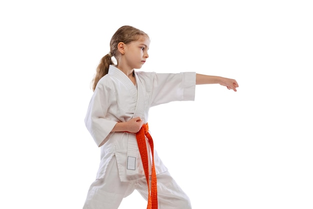 Portrait of little girl, child in kimono training karate isolated on white. Taekwondo, judo