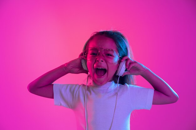 Portrait of little girl in headphones on purple gradient