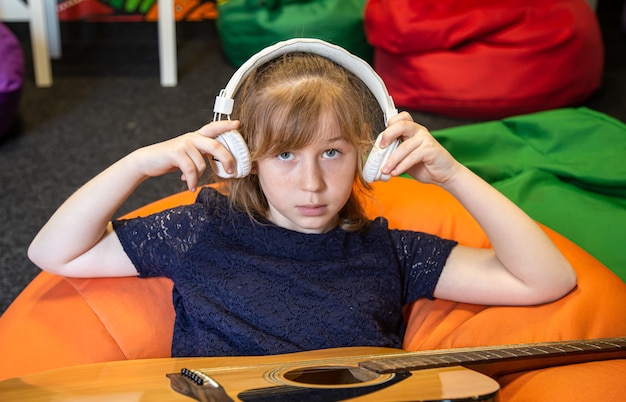 Портрет маленькой девочки в наушниках и с гитарой в процессе обучения музыке