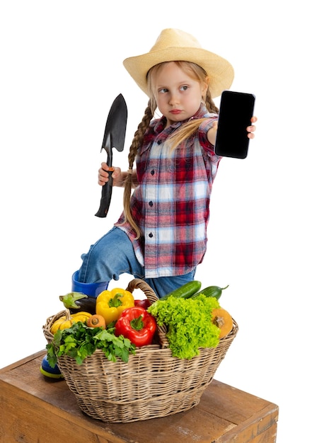 Portrait of little girl in image of farmer with large basket of vegetables isolated on white background