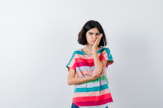 Portrait of little girl keeping hand on cheek in t-shirt and looking upset front view