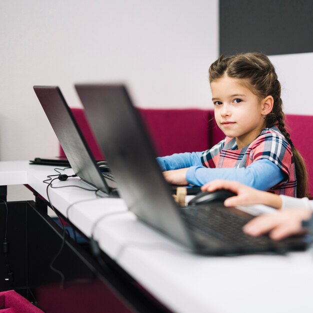 Portrait of a little girl looking at camera sitting with laptop in the classroom