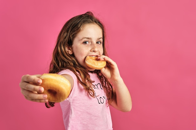 Portrait of a little girl offering a donut on a pink wall