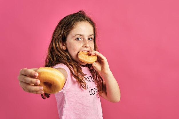 Portrait of a little girl offering a donut on a pink wall