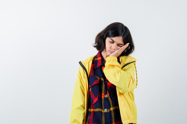 Portrait of little girl pillowing face on her hand in checked shirt, jacket and looking sleepy front view