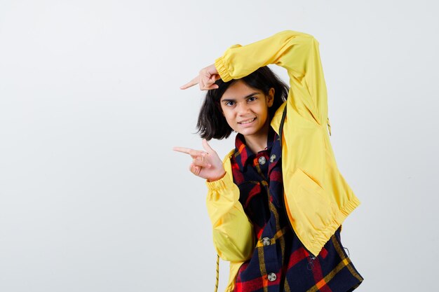 Portrait of little girl pointing to the left side in checked shirt, jacket and looking positive front view