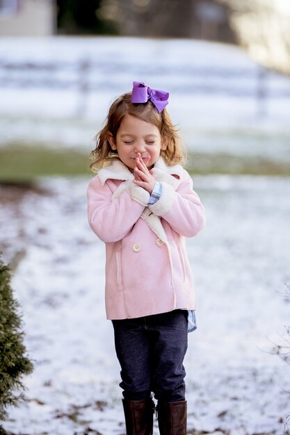 Portrait of a little girl praying in a park covered in the snow under the sunlight