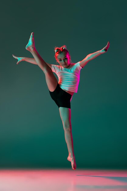 Portrait of little girl rhytmic gymnast training isolated over green background in neon lights