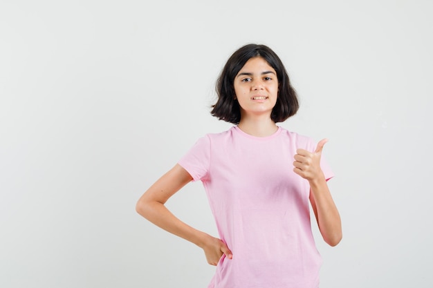 Ritratto di bambina che mostra il pollice in su in maglietta rosa e guardando allegra vista frontale