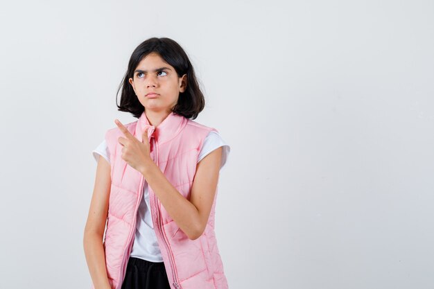 Portrait of a little girl in white t-shirt and puffer vest pointing left