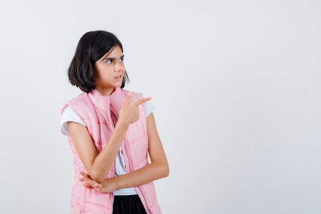 Portrait of a little girl in white t-shirt and puffer vest pointing right